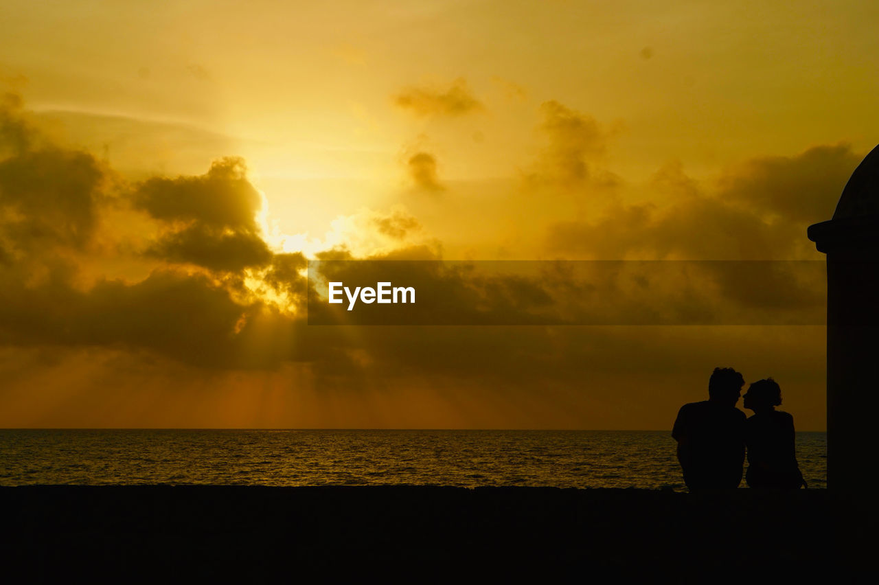 Silhouette couple on beach against orange sky