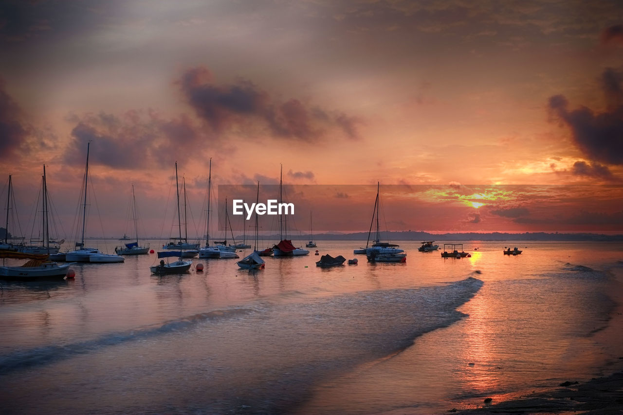 Sailboats moored on sea against sky during sunset