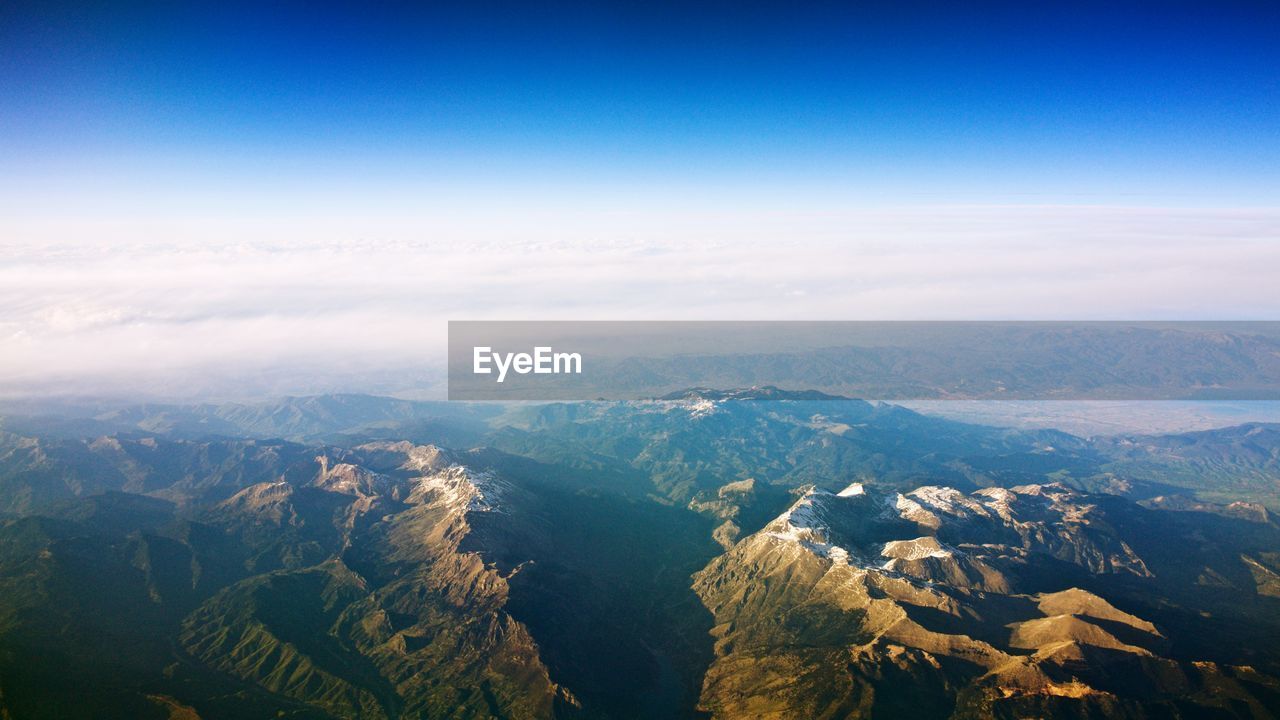 Aerial view of landscape and mountains against blue sky