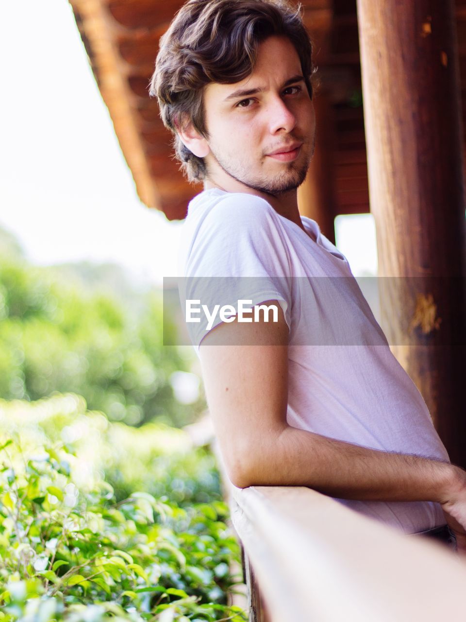 Side view portrait of young man leaning on railing by plants
