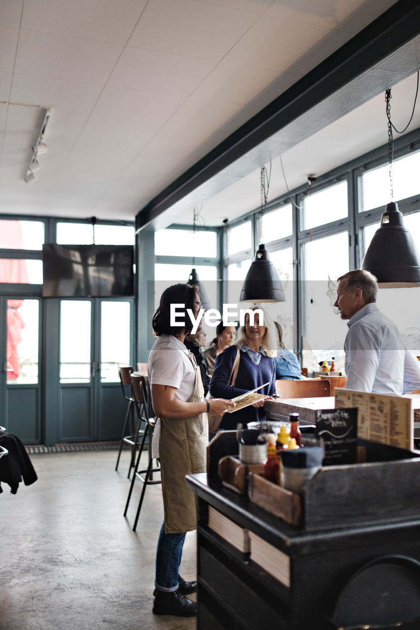 Owner showing menu cards to customers while standing at restaurant