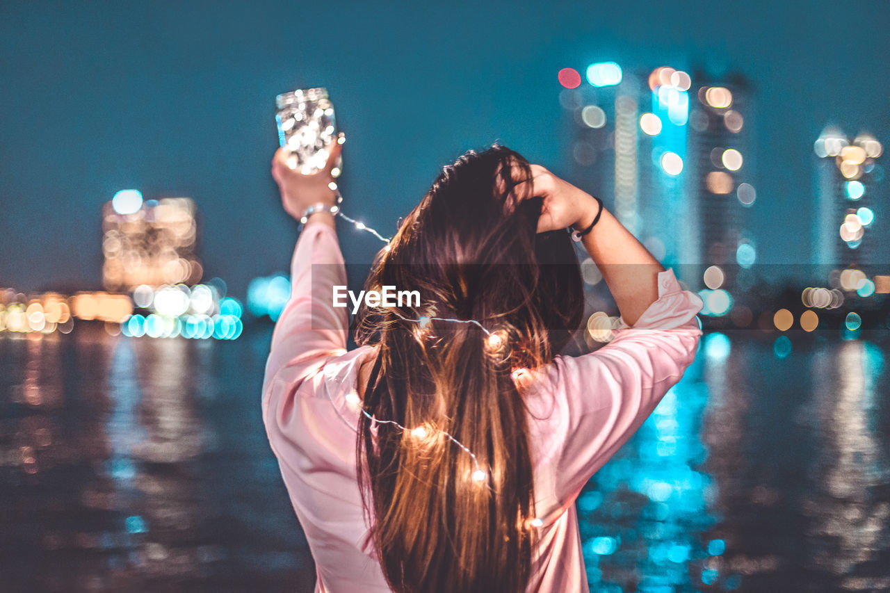 Woman standing by river in illuminated city at night