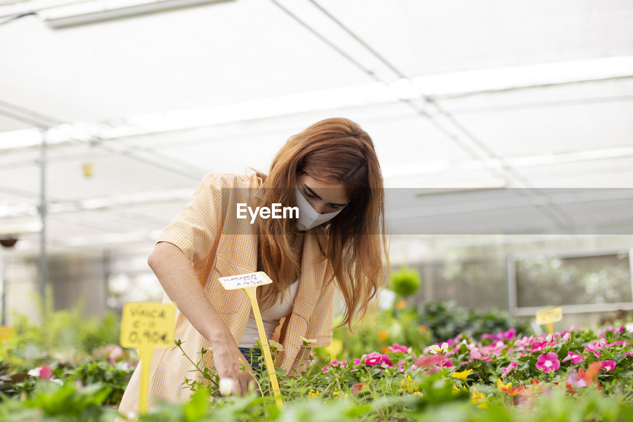Redhead businesswoman examining plant while standing at garden center