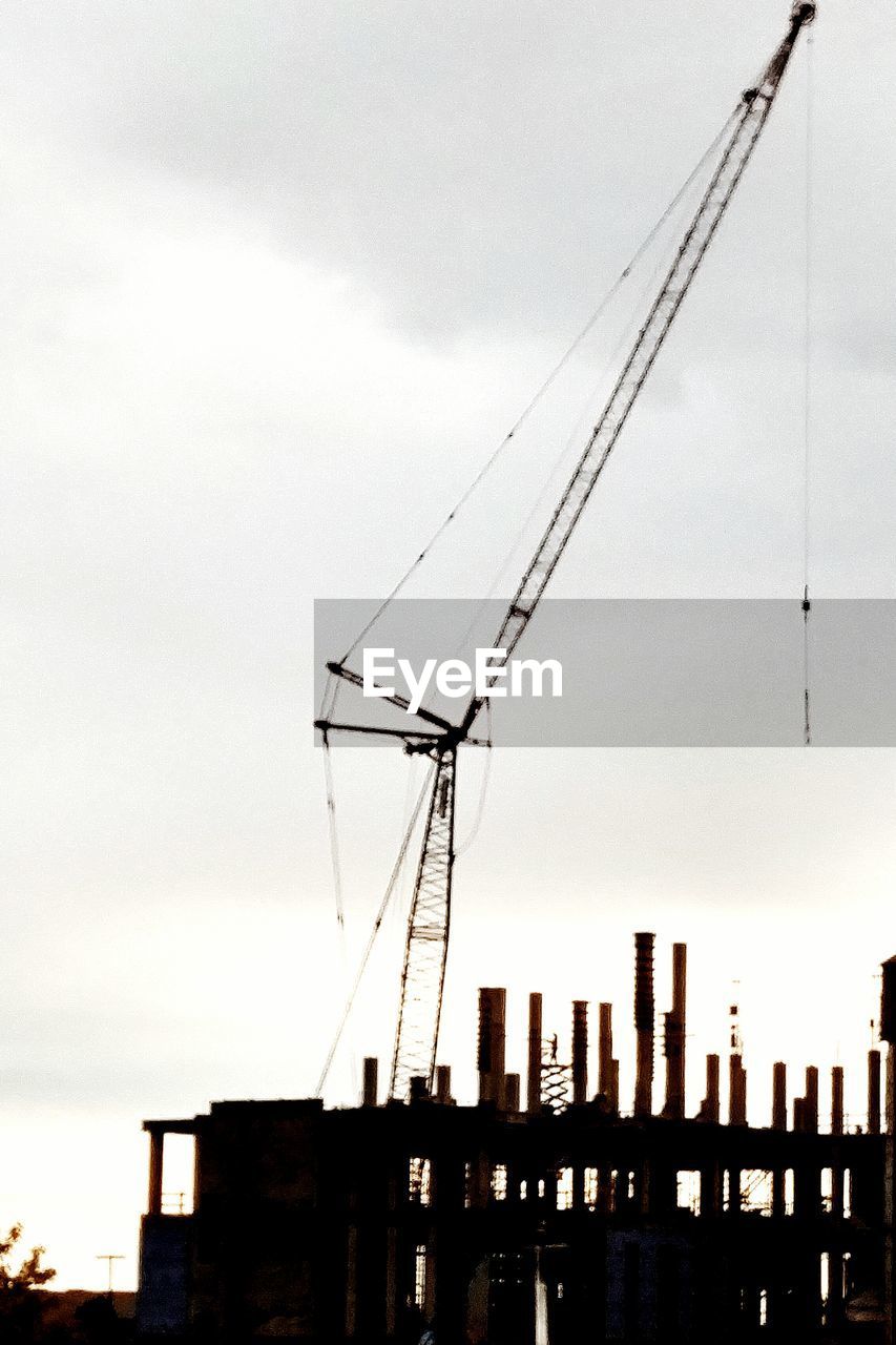 Low angle view of silhouette crane by building against sky during sunset