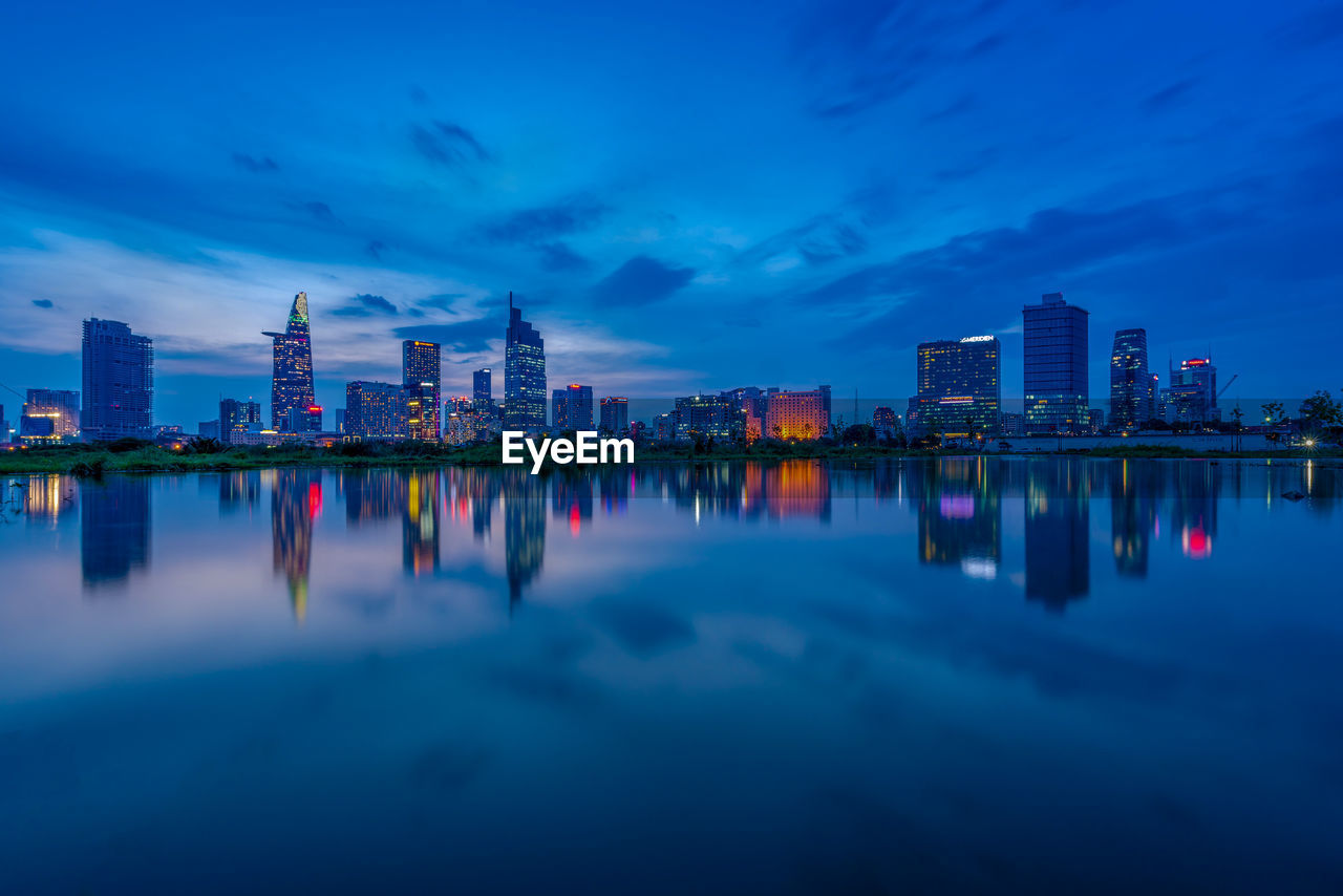 Reflection of illuminated buildings in lake against sky at dusk