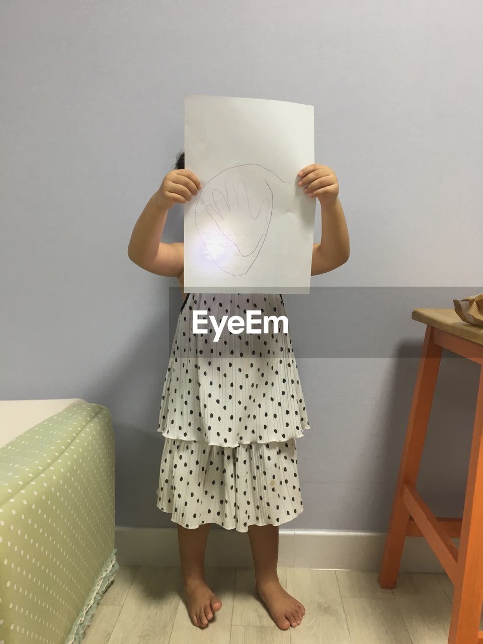 Girl covering face with drawing paper at home