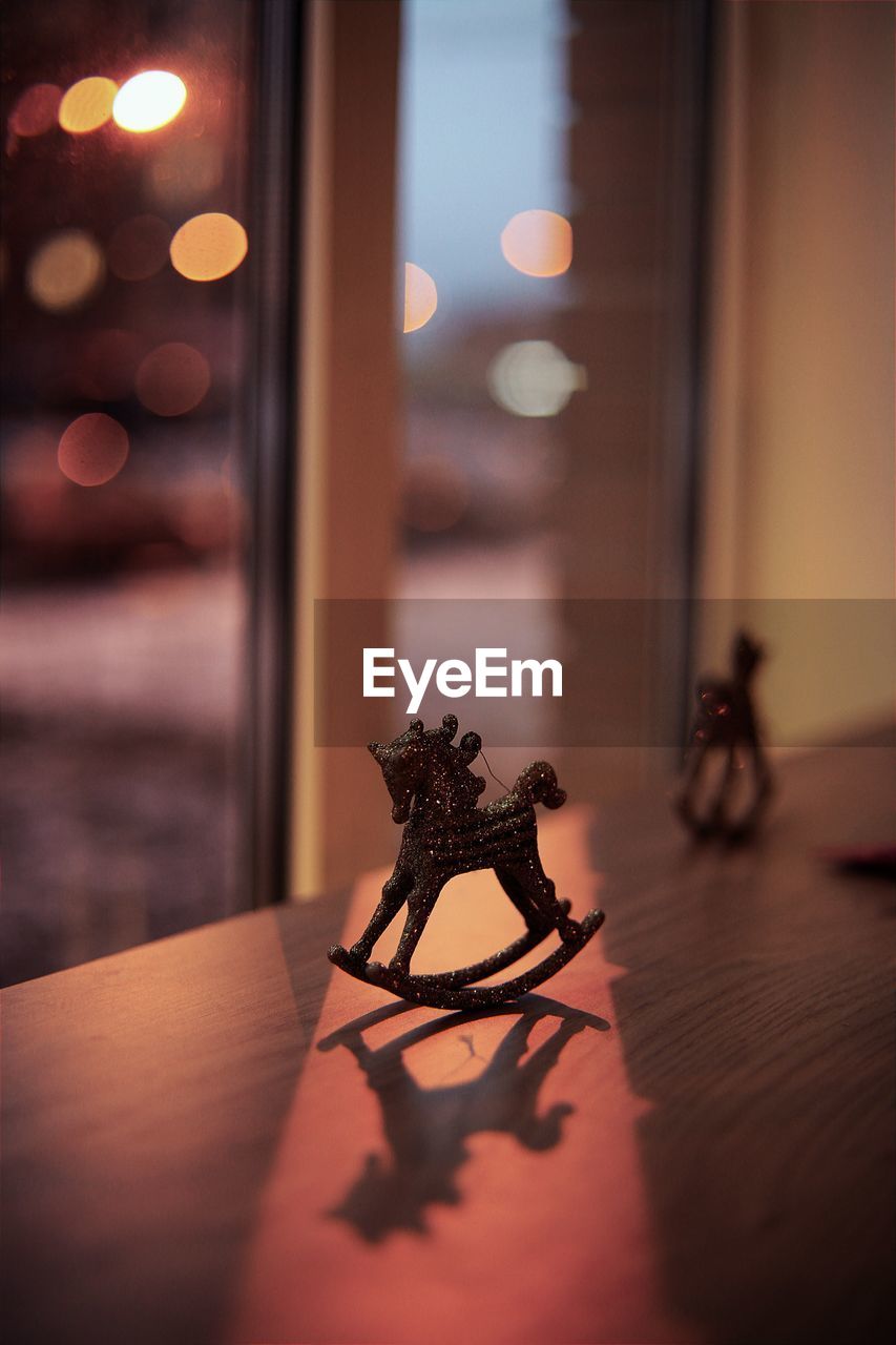 Close-up of rocking horse figurine on table against window at dusk