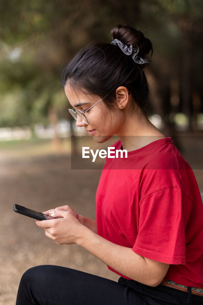 YOUNG WOMAN USING MOBILE PHONE WHILE SITTING ON CAMERA AT SMART