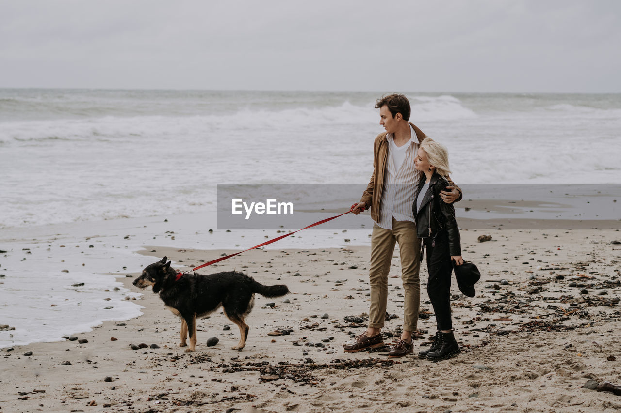 Young attractive couple having fun at he beach with a dog