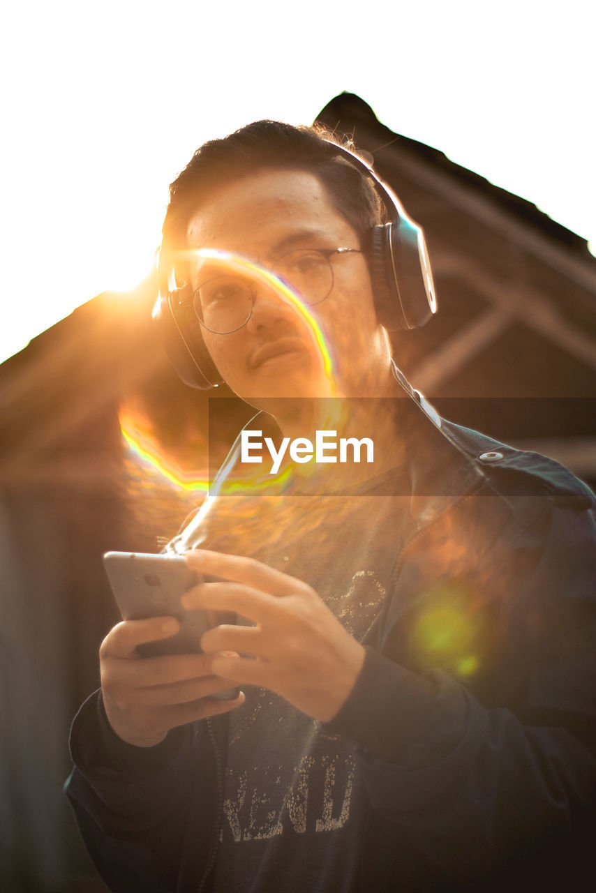 PORTRAIT OF MAN HOLDING CAMERA WHILE STANDING AGAINST SUN