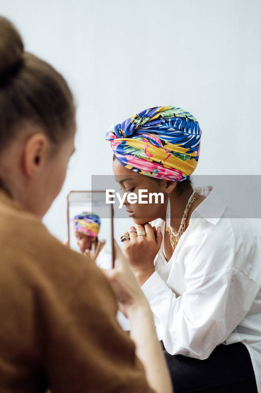 Fashion designer taking photo of young african woman model with colorful shawl on her head and