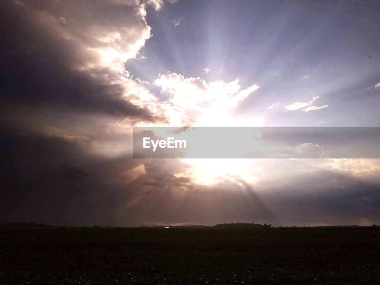 SUN STREAMING THROUGH CLOUDS OVER FIELD