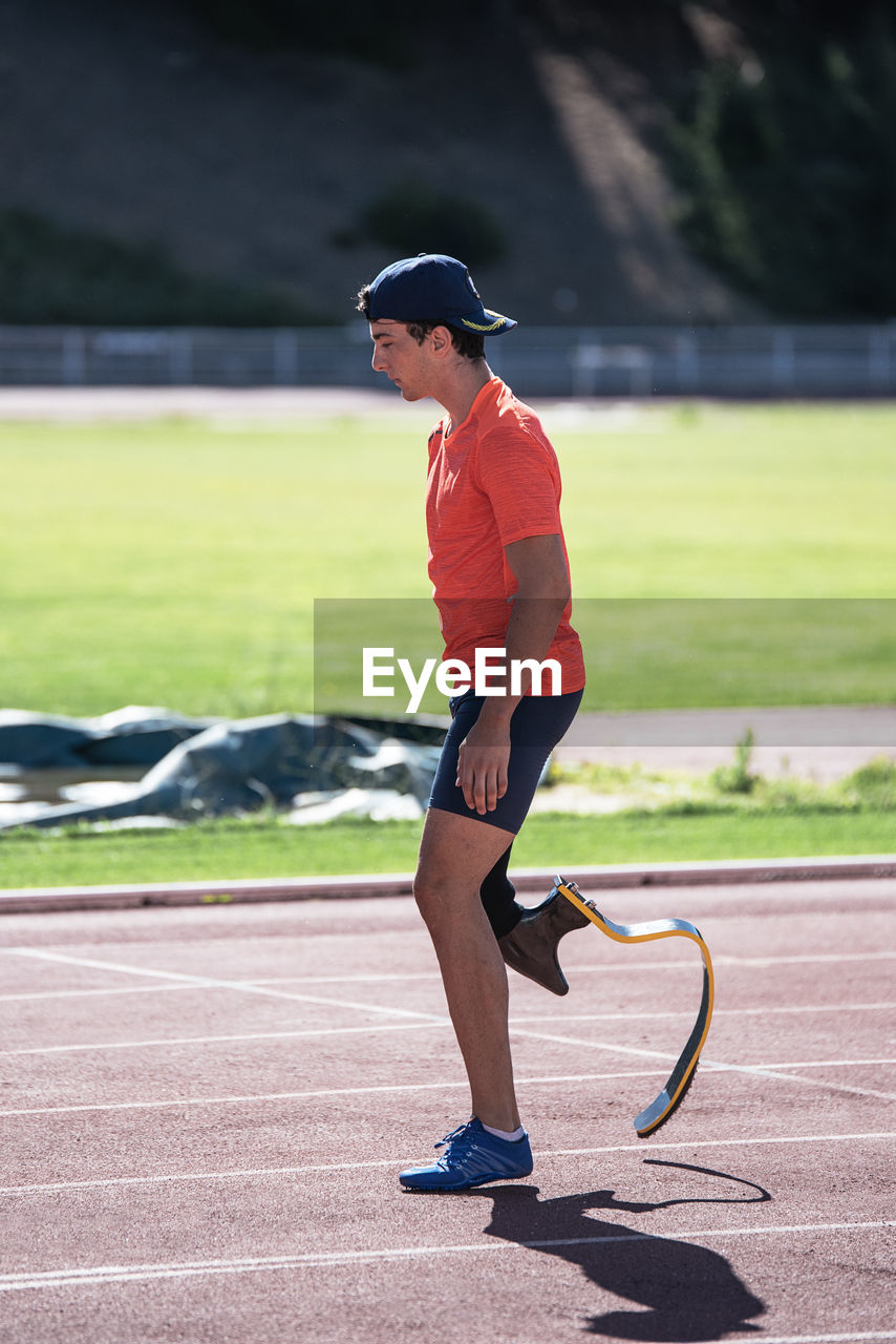 Side view of young athlete with prosthetic leg standing at sports track
