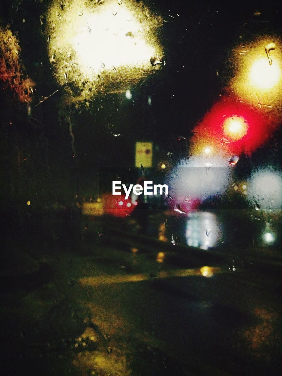 Close-up of waterdrops on glass against road at night