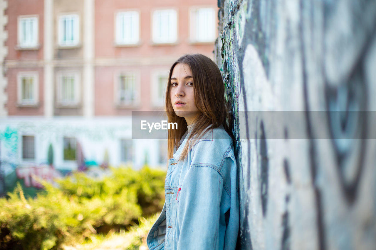 PORTRAIT OF BEAUTIFUL YOUNG WOMAN STANDING AGAINST BUILDING