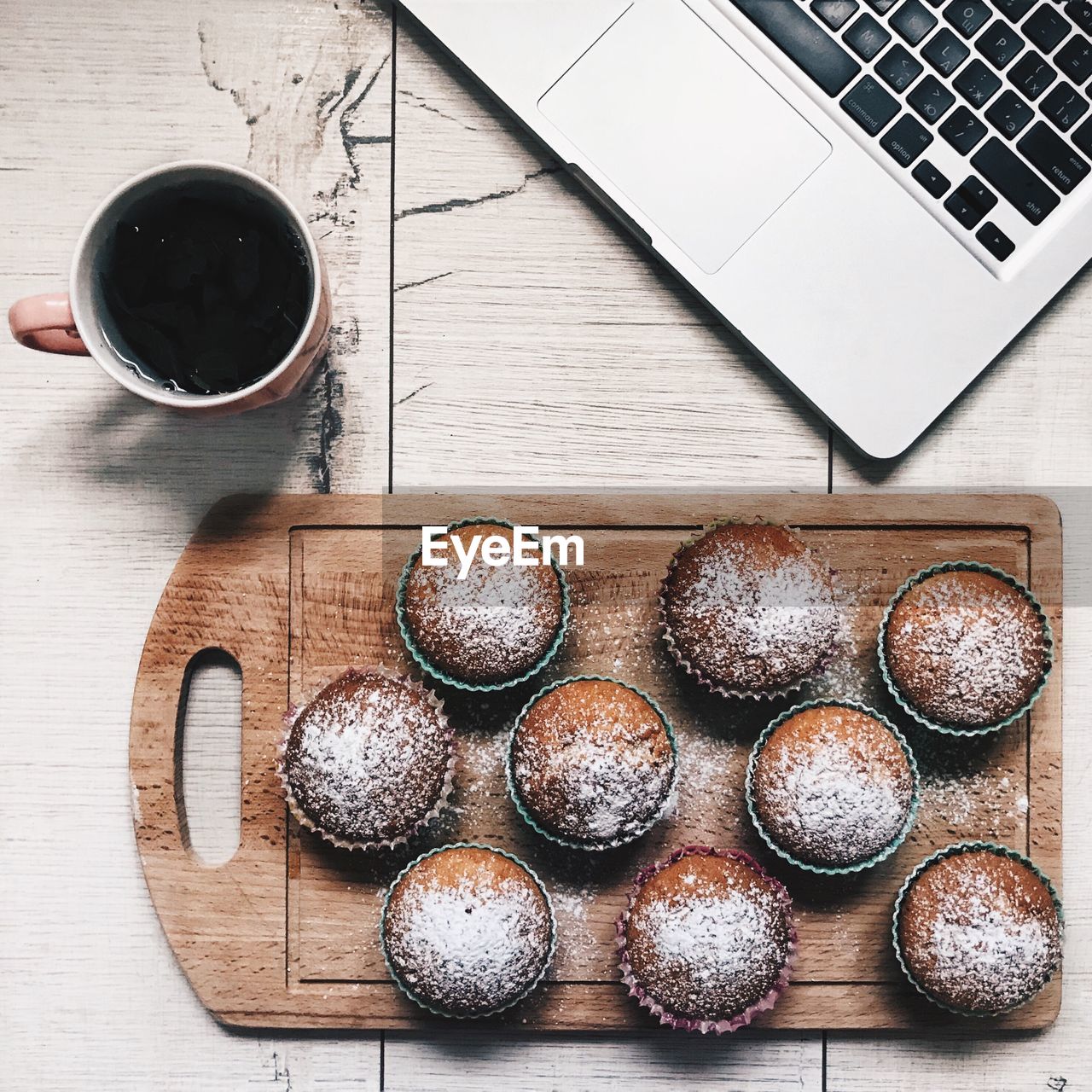 Powdered cupcakes on cutting board by black coffee over table