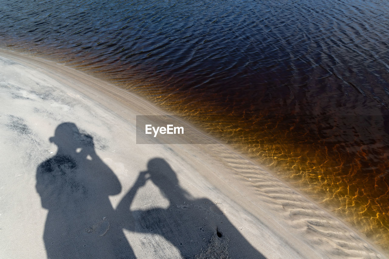 Shadows of a man and a woman on the beach sand by the water. 