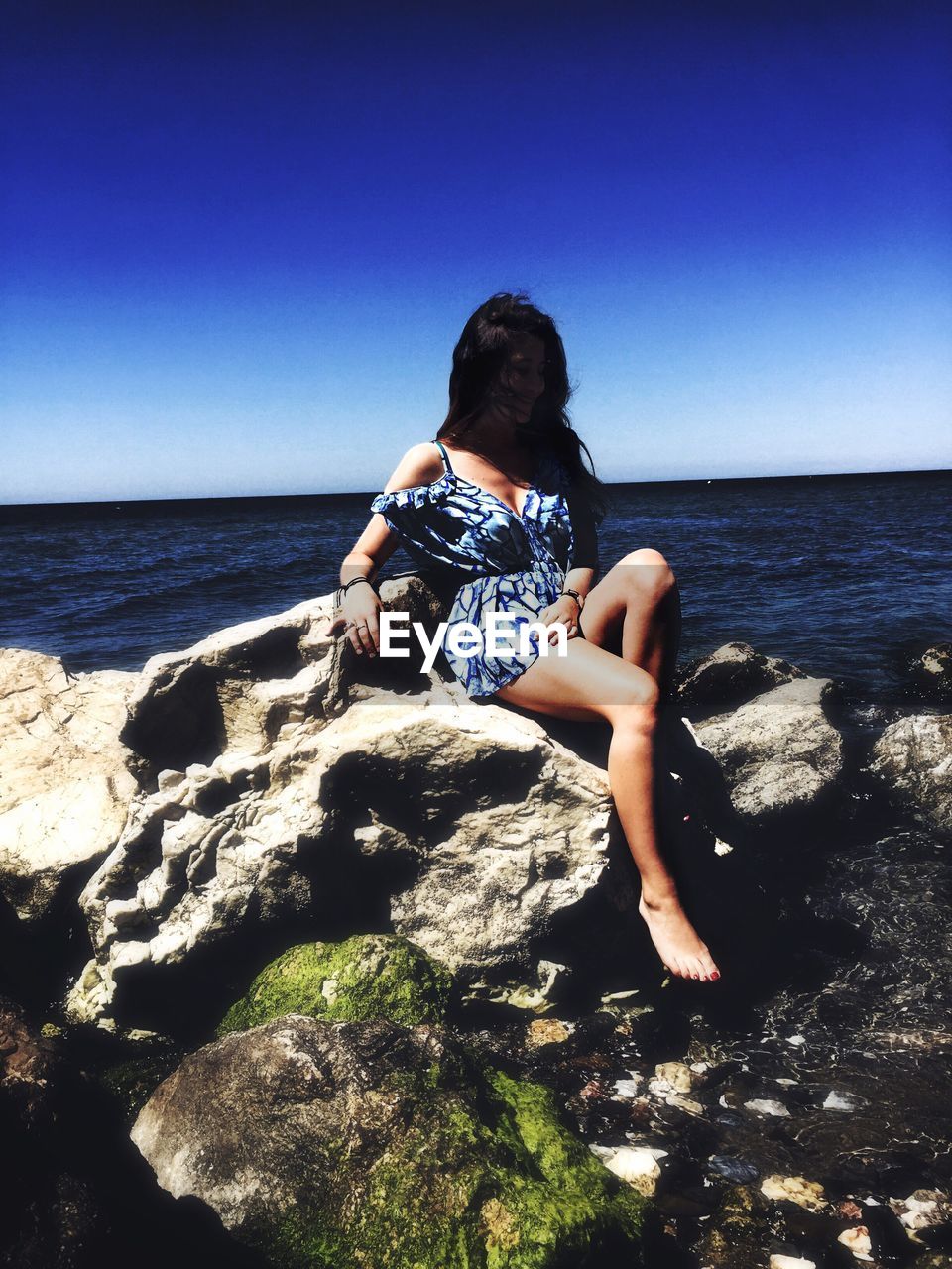 Woman sitting on rock against clear blue sky