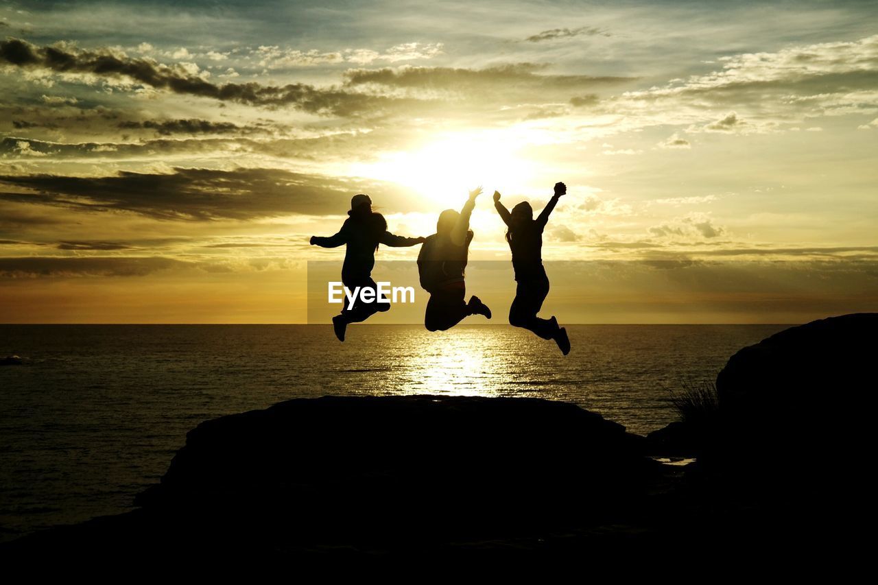 Silhouette people jumping on calm beach