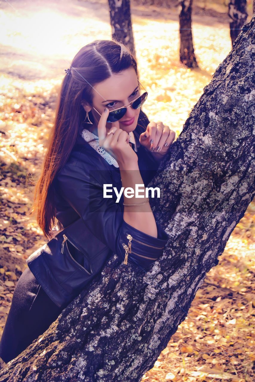 Young woman wearing sunglass by tree on field