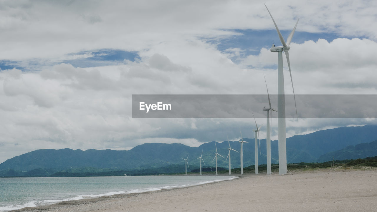 Scenic view of sea, mountains and wind turbine