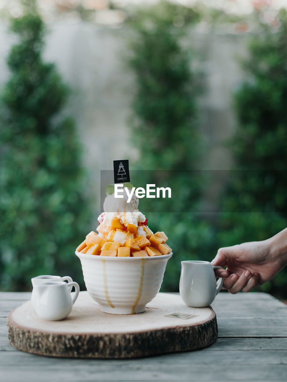 HAND HOLDING ICE CREAM IN BOWL AT TABLE