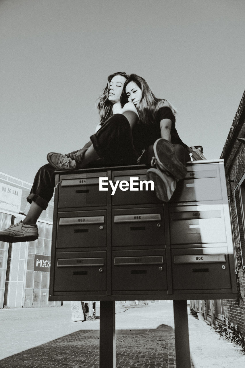 Black and white portrait of 2 women chilling on a postbox 