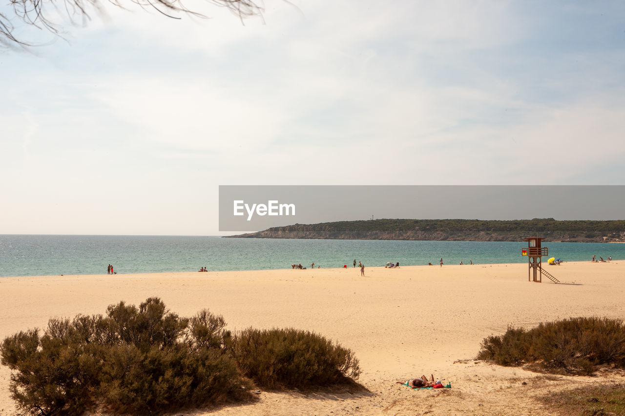 water, beach, sea, land, sky, body of water, shore, sand, nature, ocean, holiday, coast, beauty in nature, trip, vacation, scenics - nature, group of people, travel, bay, travel destinations, horizon over water, cloud, horizon, leisure activity, plant, tree, day, tranquility, men, tourism, adult, outdoors, summer, tranquil scene, lifestyles, coastline, sunlight, relaxation, women, idyllic