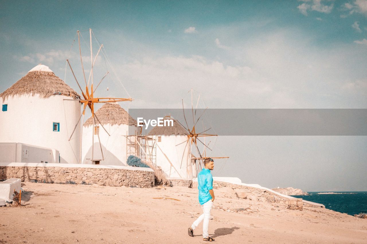 Full length of man walking at beach against sky and traditional windmills