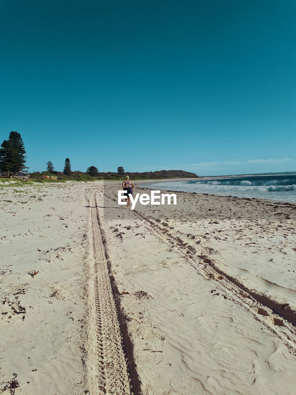 Rear view of woman running at sandy beach against blue sky