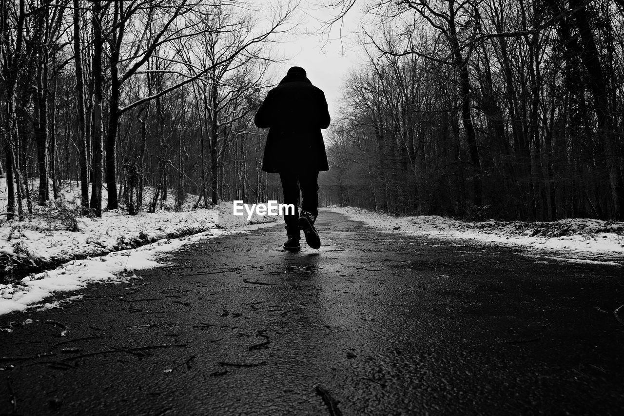 Rear view of man walking on snow road during winter
