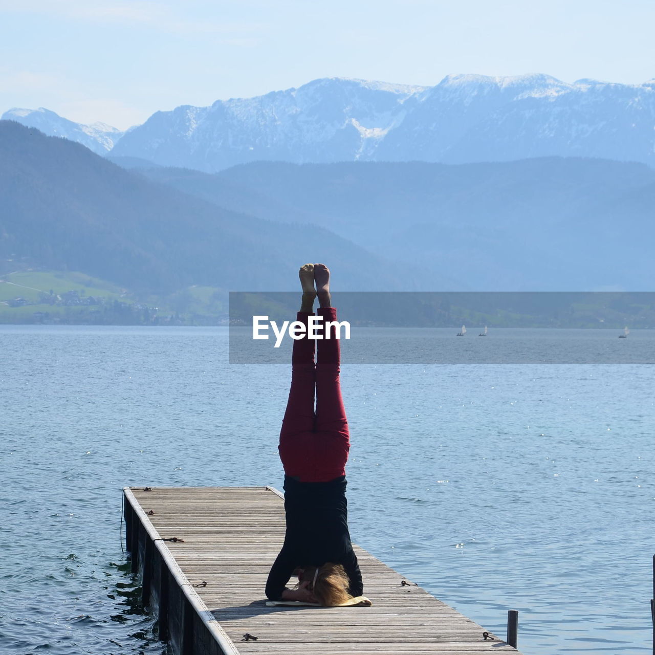 Woman exercising on pier over lake against mountains