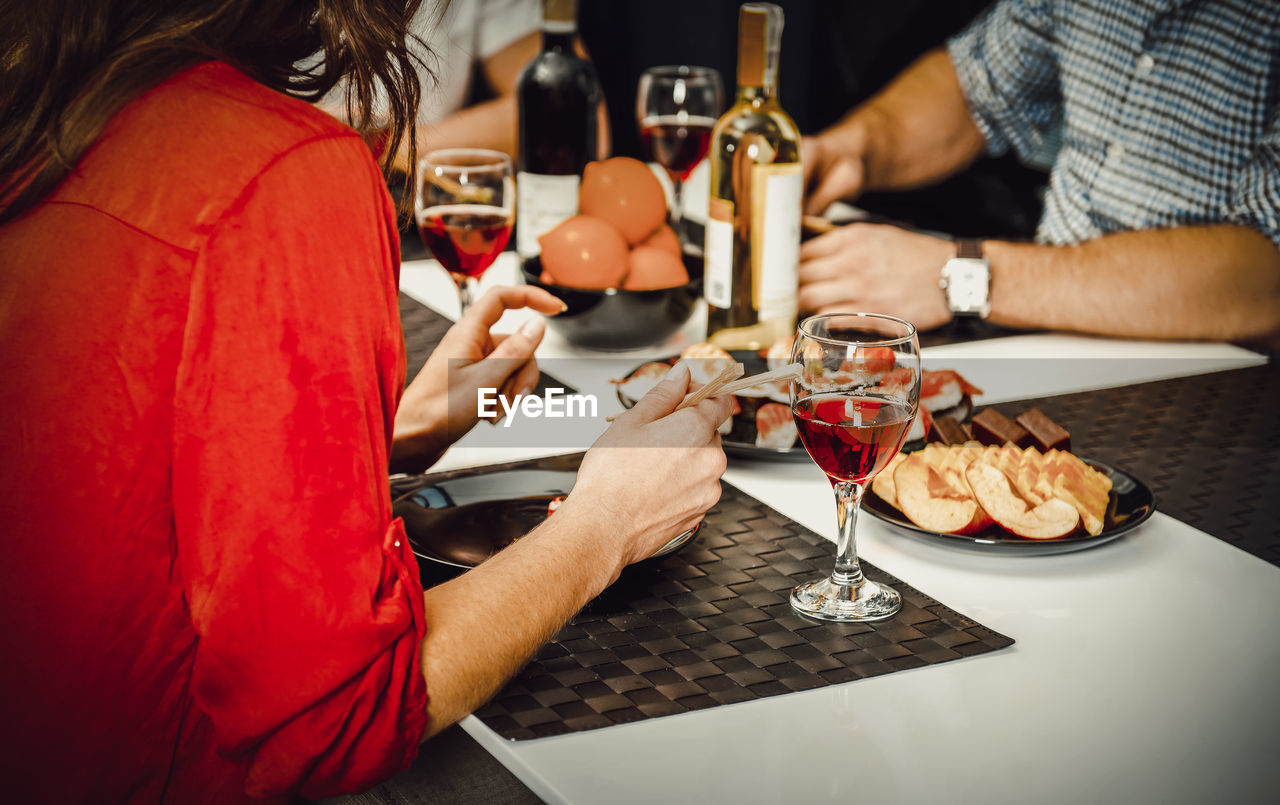 Midsection of friends having food with wine at restaurant