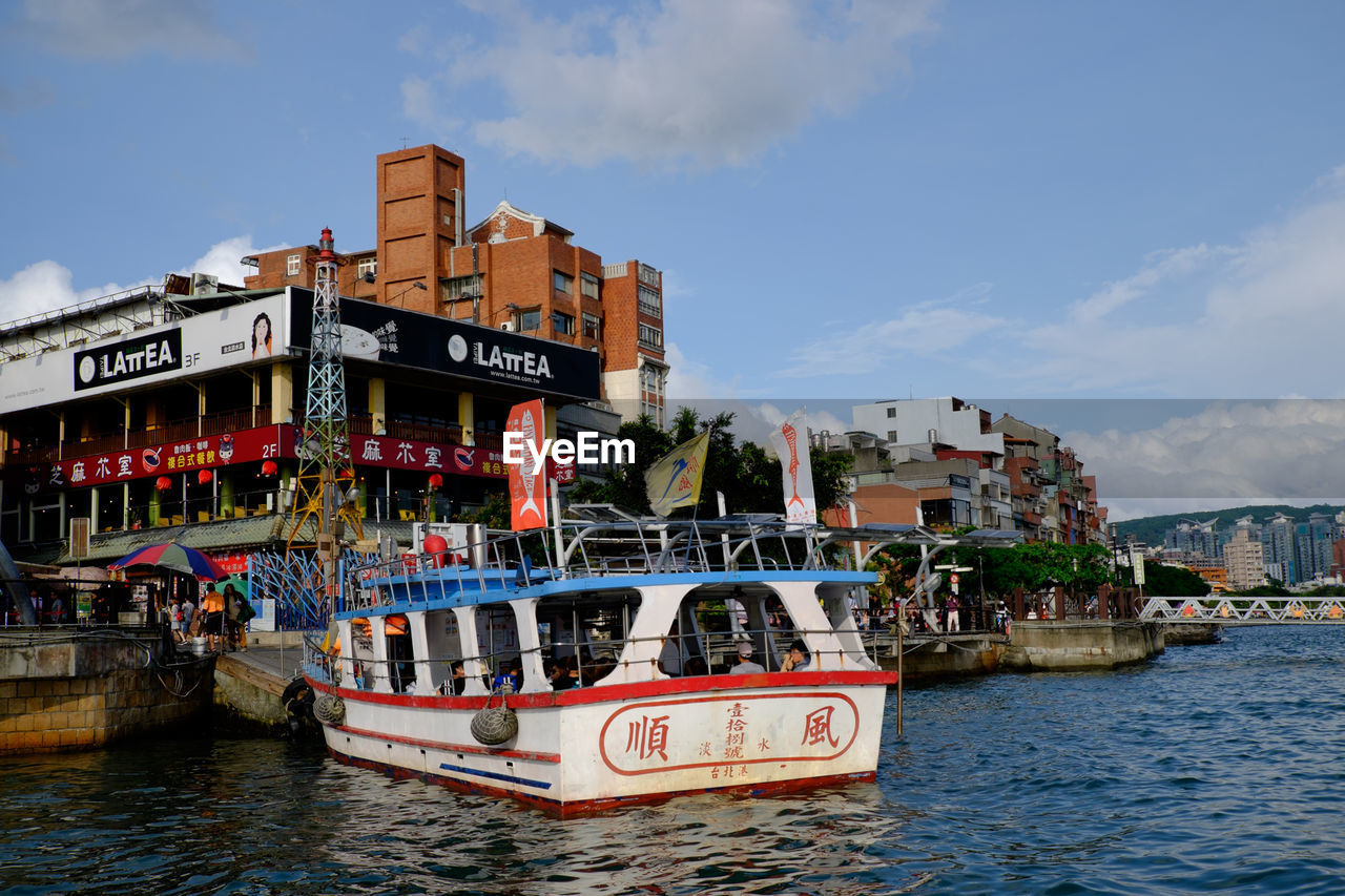 BOATS MOORED IN RIVER WITH BUILDINGS IN BACKGROUND