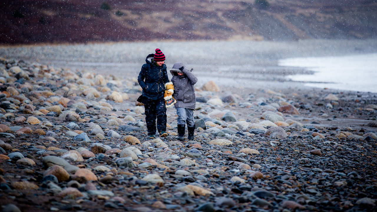Full length of mother walking with son at beach during winter