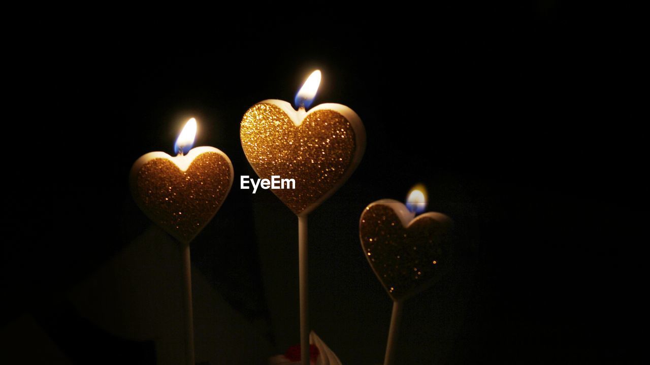 CLOSE-UP OF BURNING CANDLES AGAINST BLACK BACKGROUND