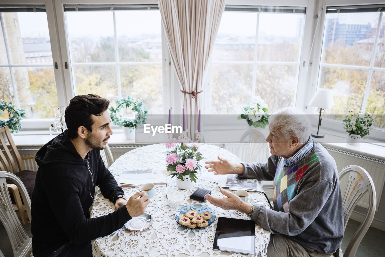Senior man talking to caretaker at dining table in nursing home