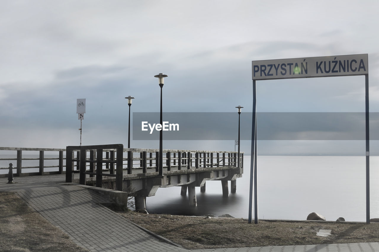 INFORMATION SIGN ON STREET BY RAILING AGAINST SKY