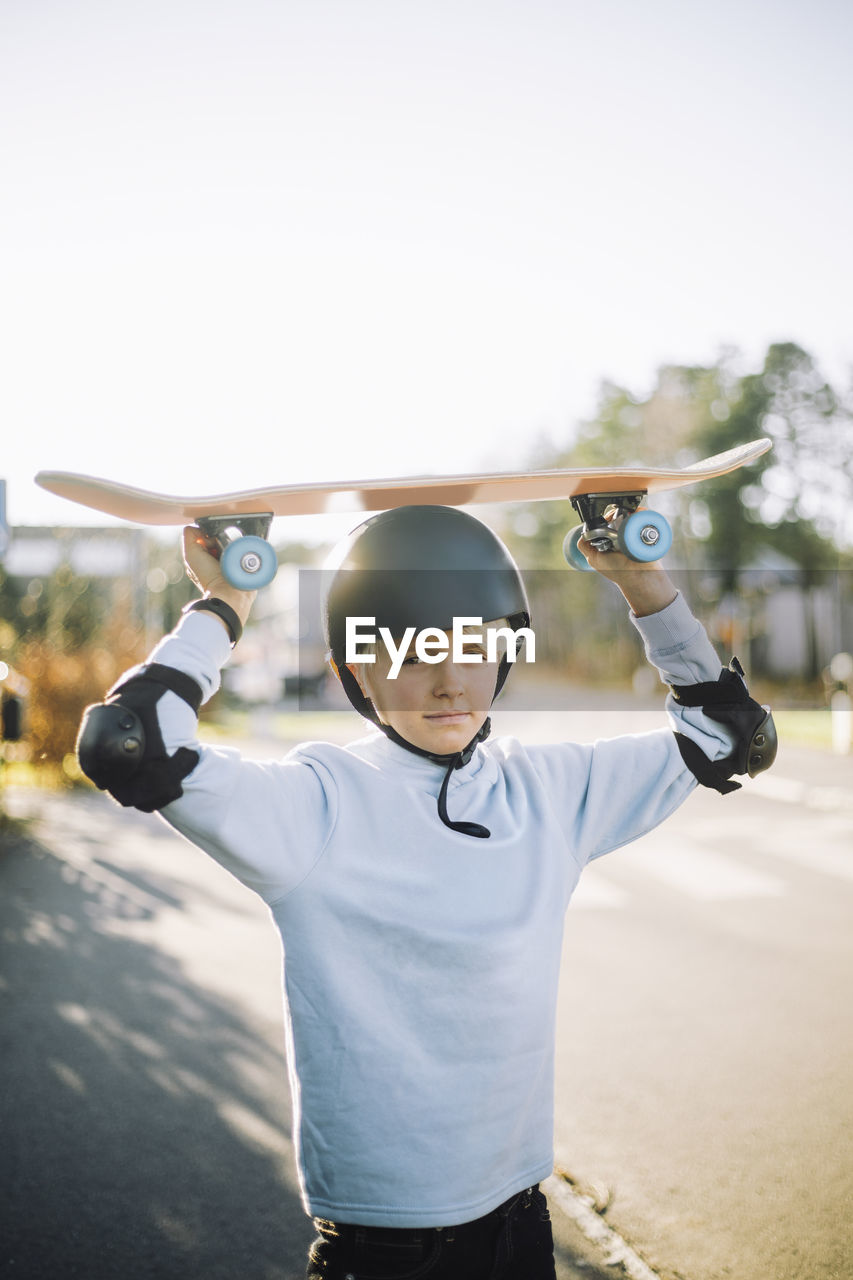 Portrait of boy carrying skateboard on head