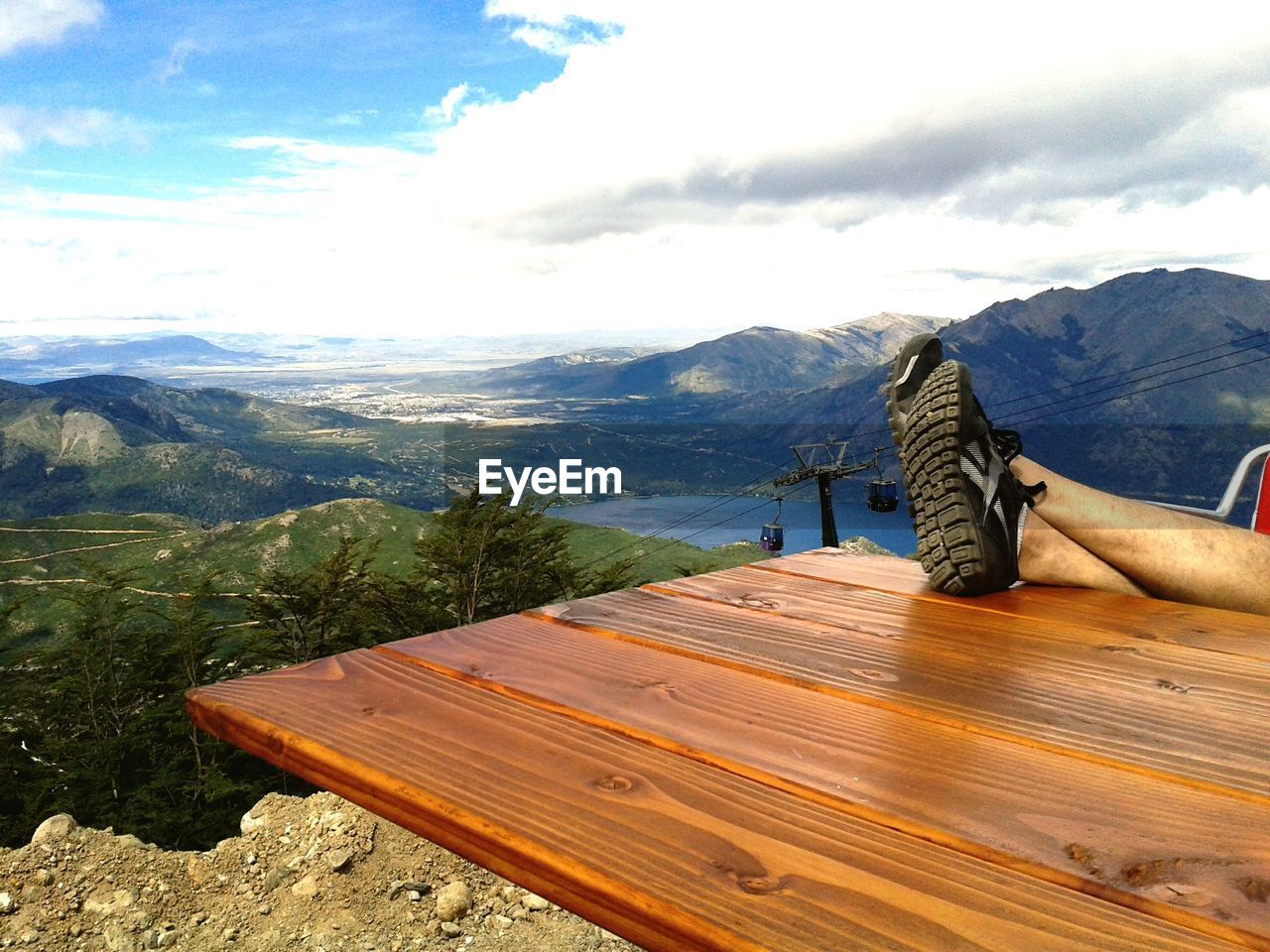 LOW SECTION OF MAN RELAXING ON WOOD AGAINST MOUNTAIN RANGE