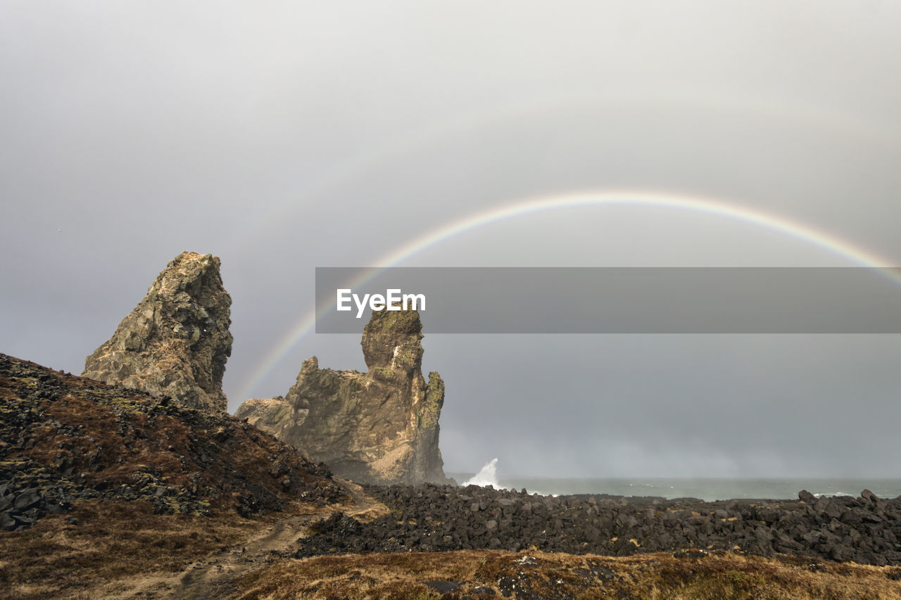 Rock formations against rainbow over sea