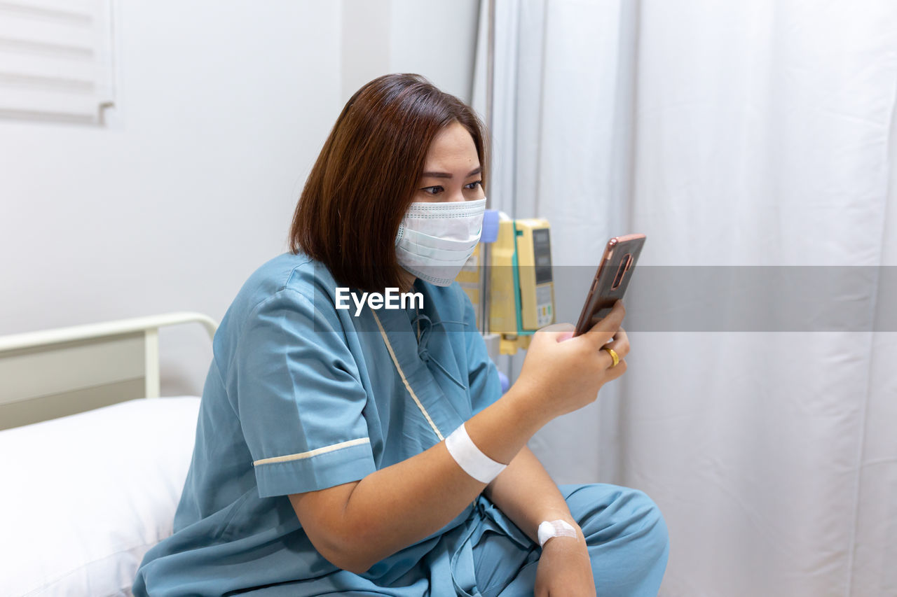 Illness asian patient women using mobile phone for checking social media in patient room of hospital