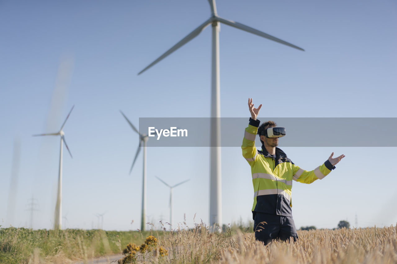 Engineer standing in a field at a wind farm wearing vr glasses