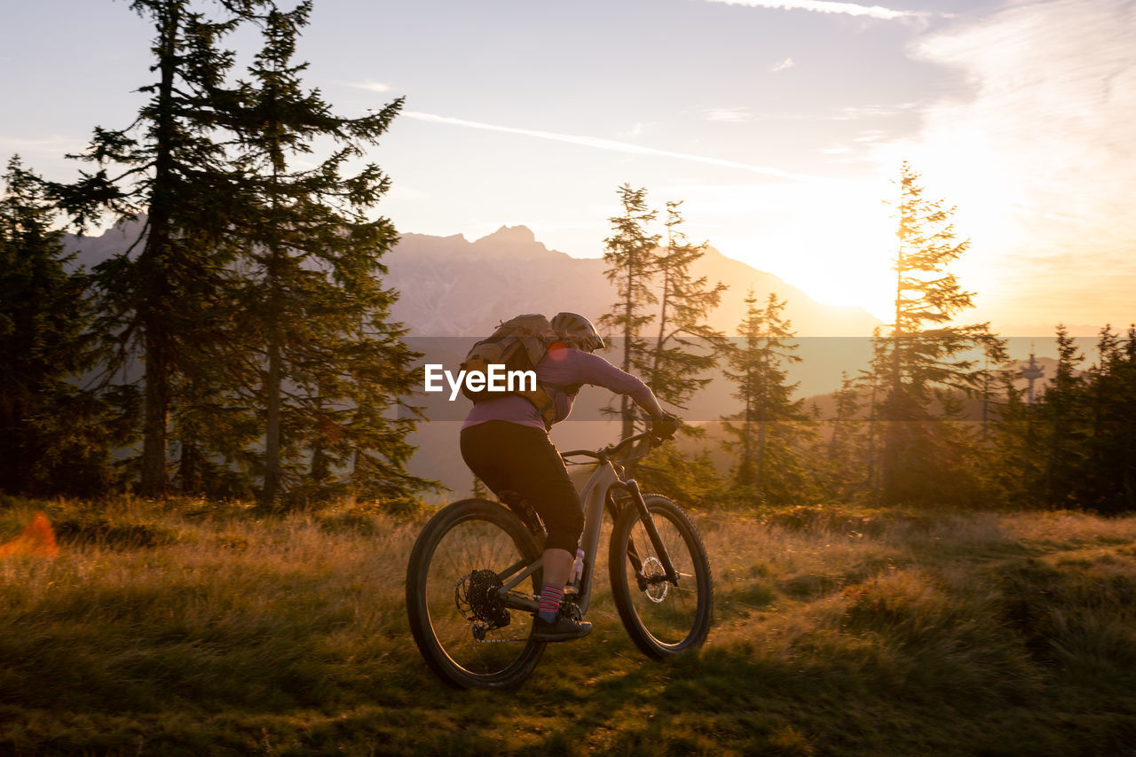  woman riding her mountain bike in early morning light on footpath, lens flare, backlight, in austria