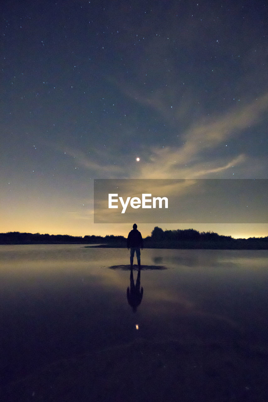 Silhouette man standing amidst lake against dusk