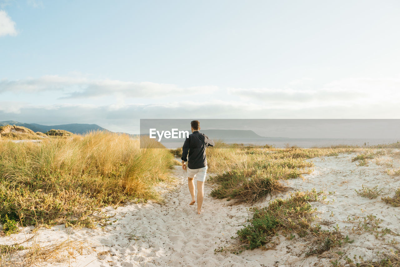 Rear view of man walking on beach against sky