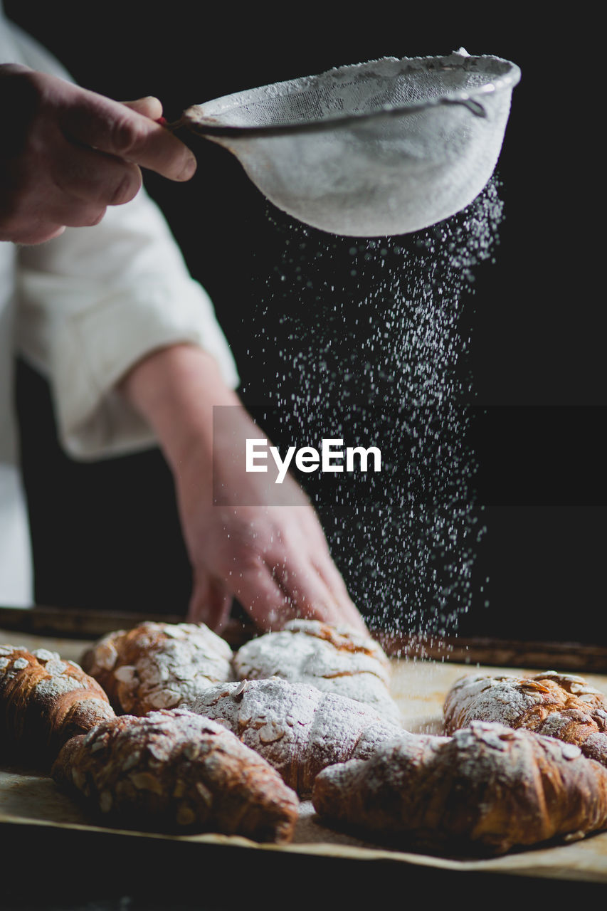 Midsection of chef sprinkling powdered sugar on croissants in bakery