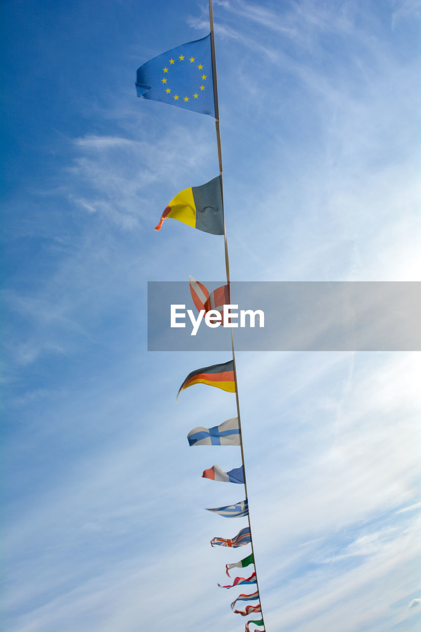 sky, blue, cloud, nature, flag, wind, low angle view, multi colored, environment, toy, day, no people, patriotism, kite sports, flying, windsports, sports, outdoors, kite - toy