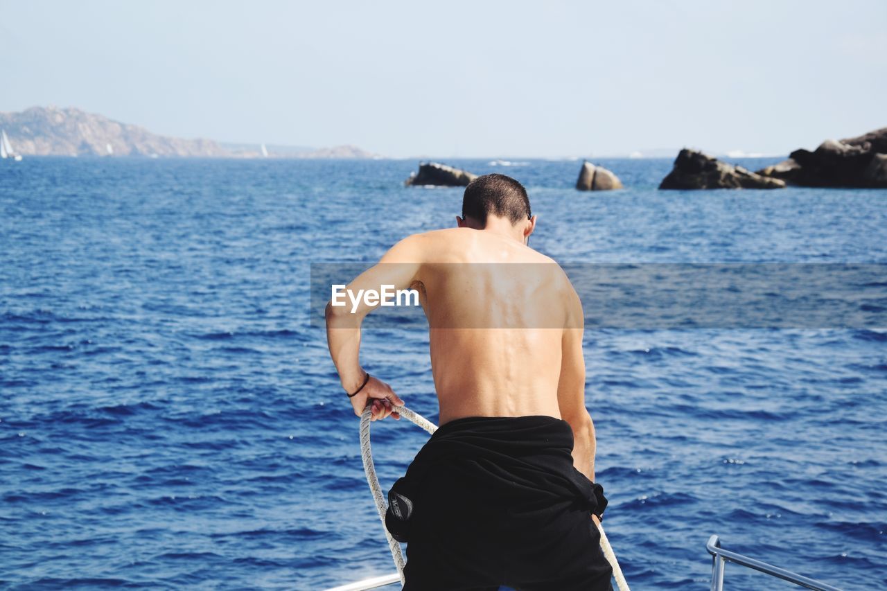 Rear view of shirtless man on boat in sea against sky