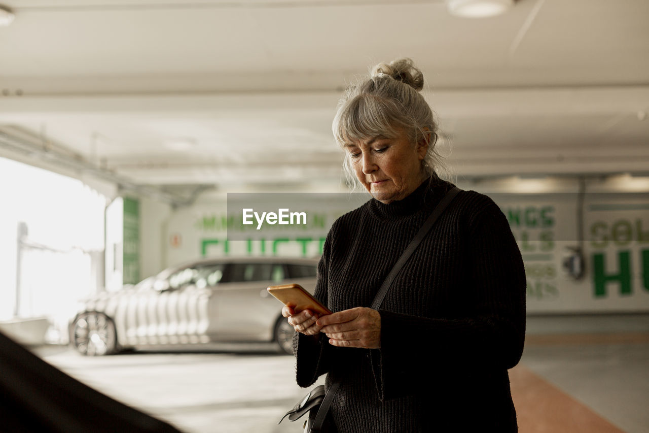 Senior woman with cell phone in parking lot